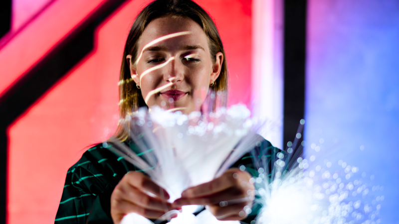 A person holds glowing fiber optic cables against a red and blue gradient background with black diagonal lines.